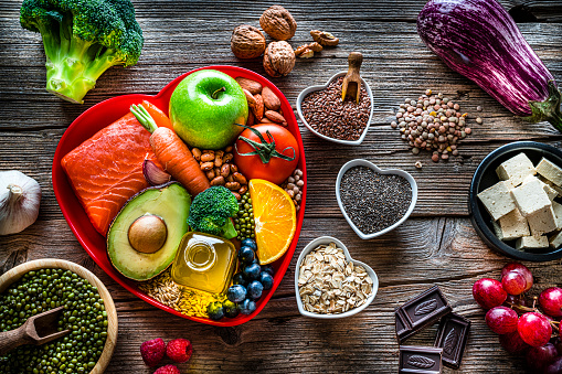 Healthy eating: group of fresh multicolored foods to help lower cholesterol levels and for heart care shot on wooden table. The composition includes oily fish like salmon. Beans like Pinto beans and brown lentils. Vegetables like garlic, avocado, broccoli, eggplant and tomatoes. Fruits like apple, grape, orange and berries. Nuts like almonds and walnuts. Soy products like tofu and soybeans. Cereals and seeds like chia seeds, flax seeds, oatmeal and barley. Olive oil, dark chocolate and yogurt with added sterols and stanols. High resolution 42Mp studio digital capture taken with SONY A7rII and Zeiss Batis 40mm F2.0 CF lens